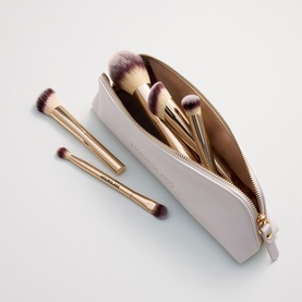 Hourglass makeup brush set with gold-handled brushes and purple tips, displayed with a pale grey zip pouch, two brushes placed beside it.