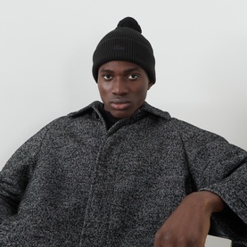 Model with Lacoste Crocodile Logo Pom Beanie Hat in black, ribbed knit with pom-pom, styled with a dark marl overshirt