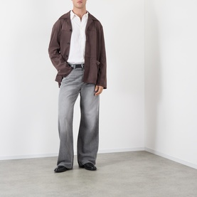 Model wearing Acne ash grey wide-leg jeans in cotton-lyocell blend, styled with a brown jacket, white shirt and black leather shoes.