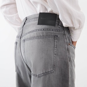 Model wearing Acne ash grey jeans, rear view showing leather logo patch on back pocket, styled with white shirt