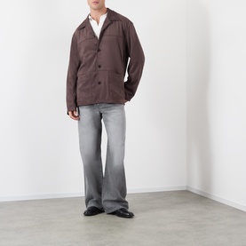 Model wearing Acne ash grey jeans in wide-leg fit, styled with a brown jacket and black leather shoes.