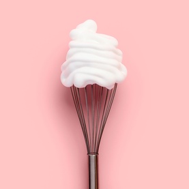 Bare by Vogue Self Tan whipped foam mousse texture shown on a silver whisk against a pink background