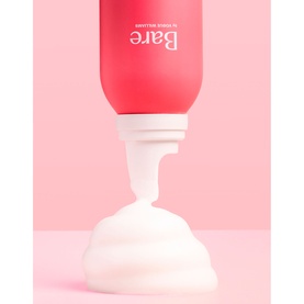 Bare by Vogue self tan gradual formula dispensing white foam from red tube on pink background
