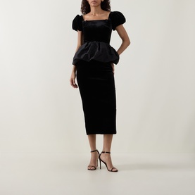 Model wearing Self-Portrait black velvet midi dress with structured peplum bodice and puff sleeves, styled with black strappy heels