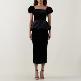 Model wearing Self-Portrait black puffed-sleeve peplum midi dress with velvet skirt, styled with black strappy heeled sandals.