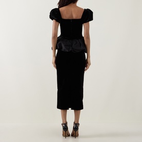 Model wearing Self-Portrait black velvet midi dress with puffed sleeves and structured floral peplum detail, back view, styled with strappy heels.