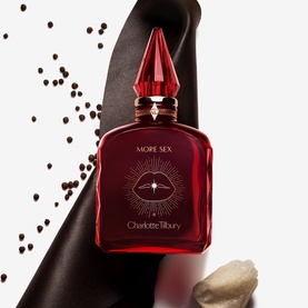 Charlotte Tilbury More Sex fragrance in deep red bottle with pointed red cap, styled with black silk and scattered peppercorns