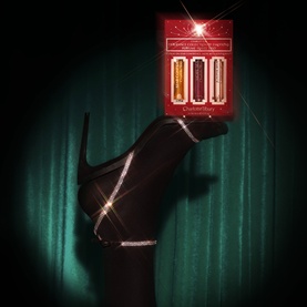 Charlotte Tilbury fragrance gift set in red presentation box, balanced on heel of a black crystal-embellished stiletto against teal backdrop.