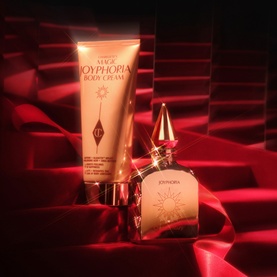 Charlotte Tilbury Magic Joyphoria Fragrance Set with body cream tube and perfume bottle in gold, styled on red satin fabric.
