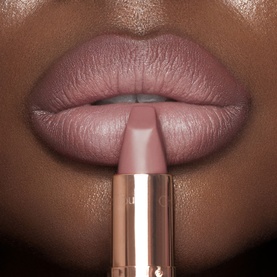 Charlotte Tilbury lipstick swatch shown on model's lips, matte nude-pink shade, gold-toned bullet visible below mouth