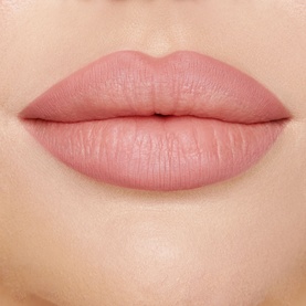 Close-up of lips wearing Charlotte Tilbury lipstick in a soft muted pink-nude shade, shown as a lip swatch beauty shot