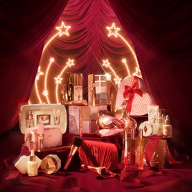 Charlotte Tilbury Beauty All makeup gift set collection displayed with festive red draping and star lights backdrop