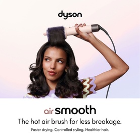 Model with Dyson Airsmooth Styling Brush, styling voluminous dark hair, brush held near head against soft gradient background.