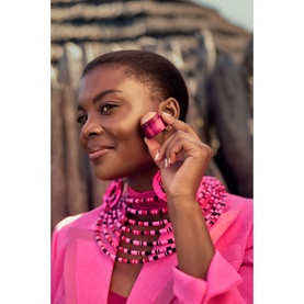 Model with Rituals balm held to cheek, wearing hot pink blazer and beaded necklace and earrings in matching pink tones