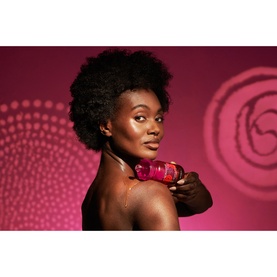 Model with Rituals shower gel held to shoulder, posed against deep pink rose-patterned background