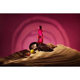 Rituals shower gel in pink bottle styled on sandy draped fabric with botanicals against a deep pink background