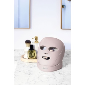 Shark Beauty CryoGlow LED Face Mask in Spa Pink, shown on marble surface with fragrance bottle and brush in background