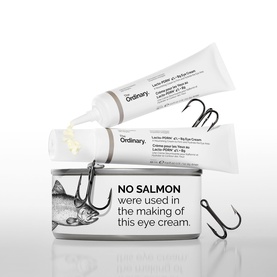 The Ordinary Eye Cream/Gel tubes displayed with branded tin and fishing hooks, highlighting salmon-free formula claim.
