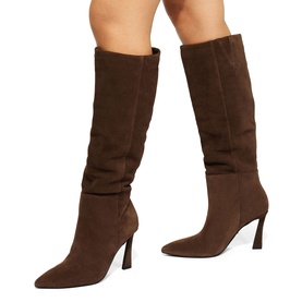 Model wearing dark brown suede knee-high heeled boots with ruched shaft, pointed toe, and stiletto heel, styled on bare legs.