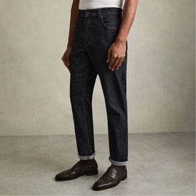 Model wearing Reiss raw indigo slim-fit jeans with turn-up hem, styled with a white tee and dark brown leather loafers