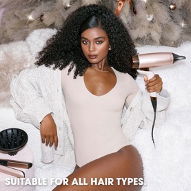 Model with GHD Deluxe Speed Hair Dryer in Cashmere Beige, styled with white fluffy cardigan and nude bodysuit, festive backdrop