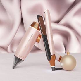 GHD Deluxe Speed Hair Dryer and Chronos Straightener Festive Gift Set in Cashmere Beige, styled with gold bauble on silk fabric