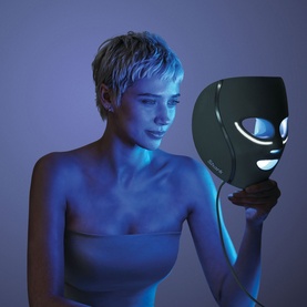 Model with Shark Beauty CryoGlow LED Face Mask Sage in green, held up to face emitting blue LED light