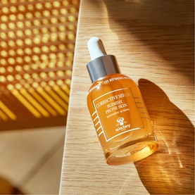Sisley Corrective Serum Blemish Prone Skin in amber glass dropper bottle, styled on wooden surface in warm sunlight.
