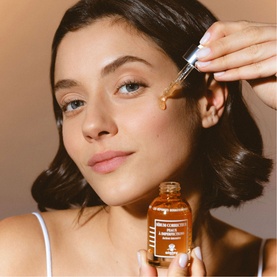 Model with Sisley Corrective Serum Blemish Prone Skin, holding amber glass dropper bottle, applying serum to cheek