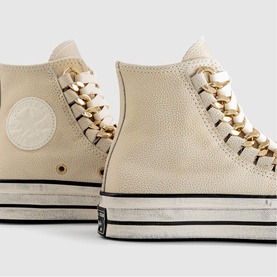 Converse Chuck 70 high-top trainers in egret pebbled leather with gold chain laces and black platform sole, close-up detail view.