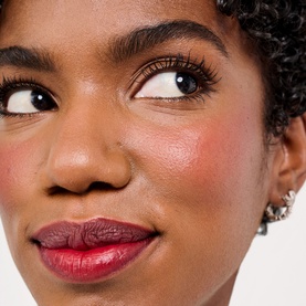 Model wearing Benefit Beauty All advent calendar makeup look featuring deep berry lip colour and rosy blush, with crystal earrings