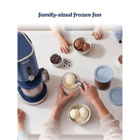 Ninja Ice Cream Maker 11-in-1 in navy blue, shown in use on a table with scooped ice cream and toppings in bowls