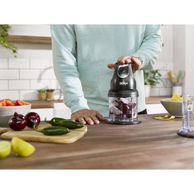 Model with Ninja Stackable Chopper 200W Black in use on kitchen counter, filled with red onion, with fresh vegetables alongside