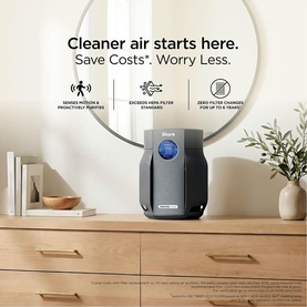 Shark air purifier in dark grey, displayed on wooden dresser beside plant, with "Cleaner air starts here" lifestyle campaign text overlay