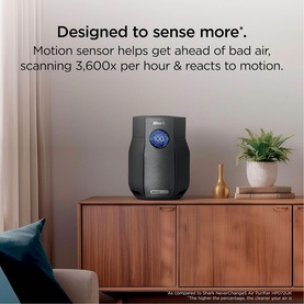 Dark grey cylindrical air purifier with circular blue LED display, shown on wooden sideboard beside houseplant in styled living room setting