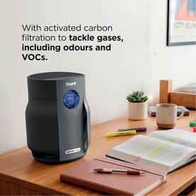 Shark air purifier in dark grey with LCD display, shown on desk beside books, highlighting activated carbon filtration for gases and VOCs