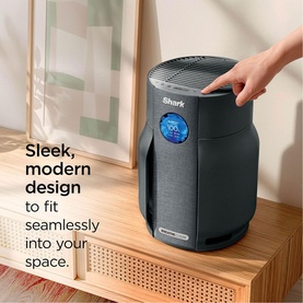 Shark Breathe Clear Compact Charcoal air purifier in dark grey with blue display, hand pressing top control on wooden sideboard