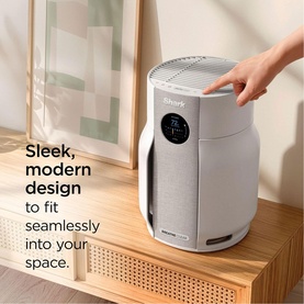 Shark Breathe Clear Compact Dove air purifier in light grey, shown on wooden shelf with hand touching top controls