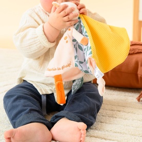 Baby holding Sophie the Giraffe multi-coloured comforter toy with yellow and floral fabric panels and orange teether tag