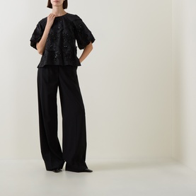 Model wearing FeeG black sequin embellished short-sleeve top, styled with wide-leg black trousers and pointed heels.
