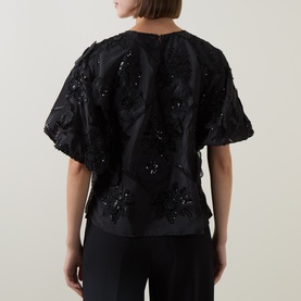 Model wearing FeeG black polyester top, back view, with 3D floral appliqu&eacute; and sequin embellishment, short puff sleeves.