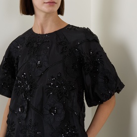 Model wearing FeeG black polyester top with floral sequin and bead embellishment, puff sleeves, close-up detail view.