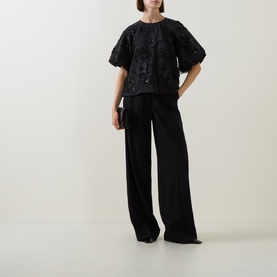 Model wearing FeeG black polyester top with floral sequin embroidery and puffed sleeves, styled with wide-leg black trousers.