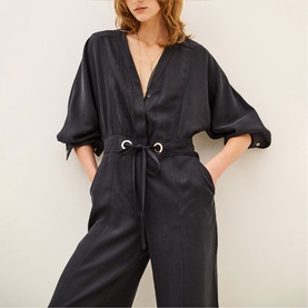 Model wearing Bash grey jumpsuit with V-neckline, elasticated waist tie, short sleeves, and wide-leg trousers