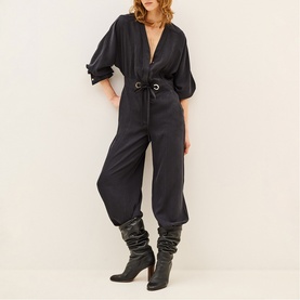 Model wearing Bash grey jumpsuit with deep V-neck, blouson sleeves and belted waist, styled with black knee-high boots