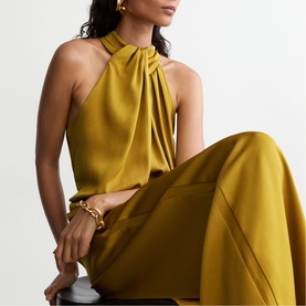 Model wearing Reiss chartreuse green halterneck dress with draped neckline, paired with gold jewellery