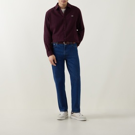 Model wearing Lacoste Oxalis casual shirt in burgundy cotton, styled with mid-blue straight-leg jeans and white trainers