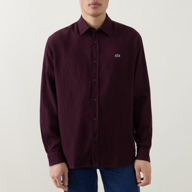 Model wearing Lacoste Casual Shirt in Oxalis burgundy, button-through front, classic collar, crocodile logo patch, styled with blue jeans.