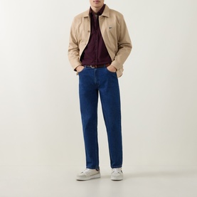 Model wearing Lacoste Oxalis casual shirt in burgundy, styled with beige jacket, blue jeans and white trainers
