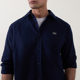 Model wearing Lacoste navy blue cotton casual shirt with button placket and embroidered crocodile logo, styled over white crew-neck tee